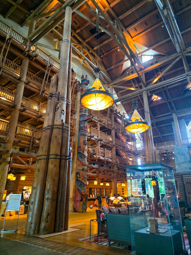 Grand lobby of Disney’s Wilderness Lodge with towering log beams, totem poles, and warm lantern lighting.