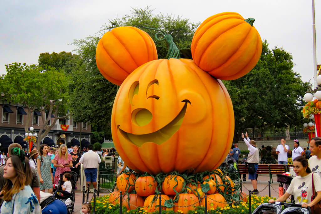 Giant winking Mickey jack-o’-lantern in Town Square on Main Street, U.S.A., surrounded by smaller pumpkins and park guests.
